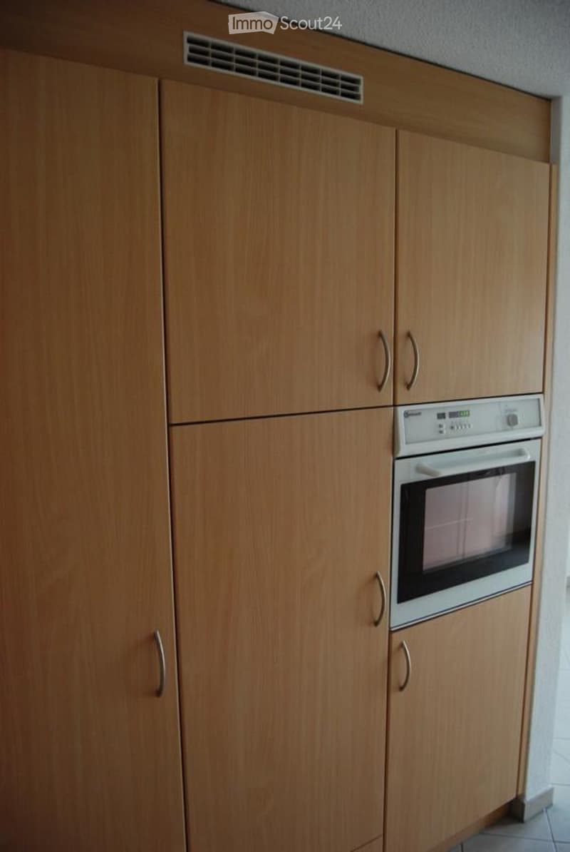 Modern kitchen with light wood cabinets and a built-in oven. The cabinets have silver handles and a sleek design.