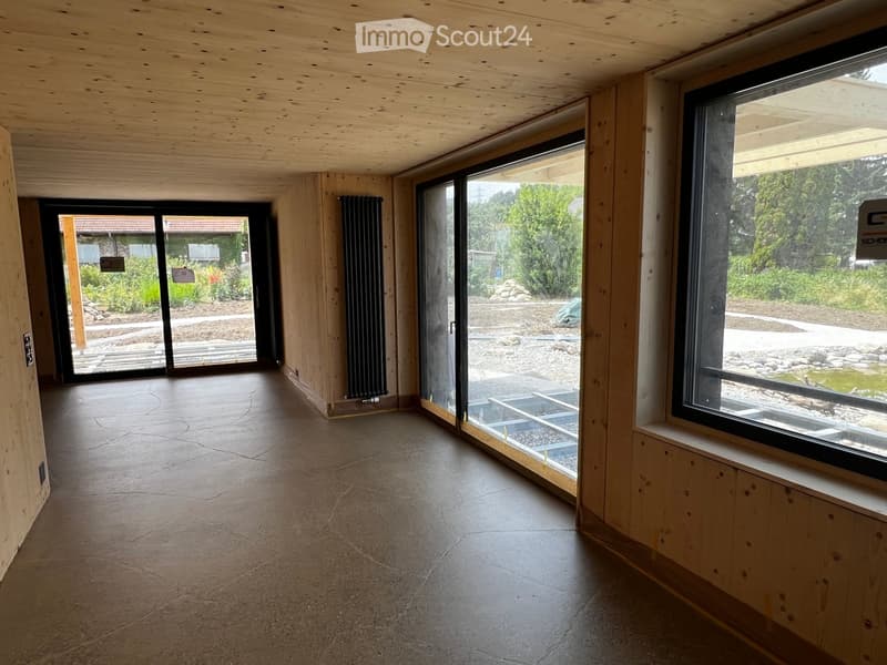 Empty room with wooden ceiling, concrete floor, large windows, and sliding glass doors leading to an outdoor area.