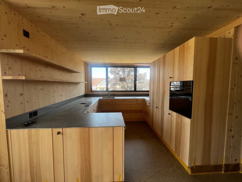 Modern kitchen with wooden cabinets, black countertop, and a large window overlooking the outside.