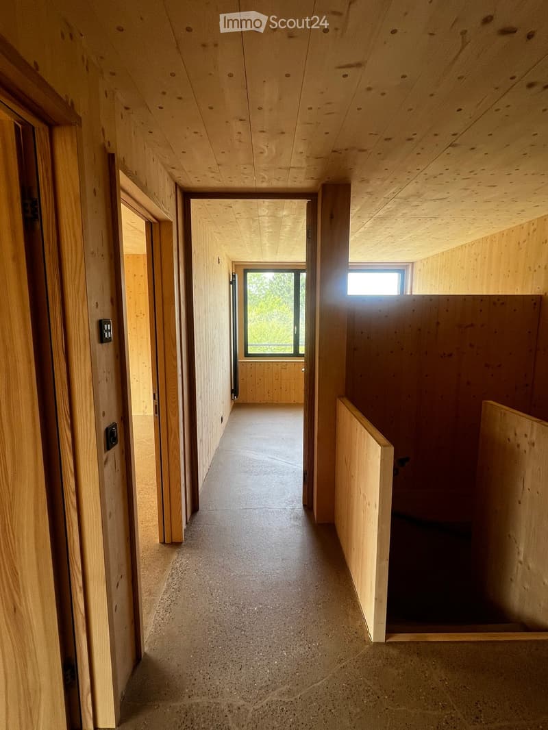 A long, narrow hallway with wooden walls and ceiling, concrete floor, and several doors leading to other rooms.