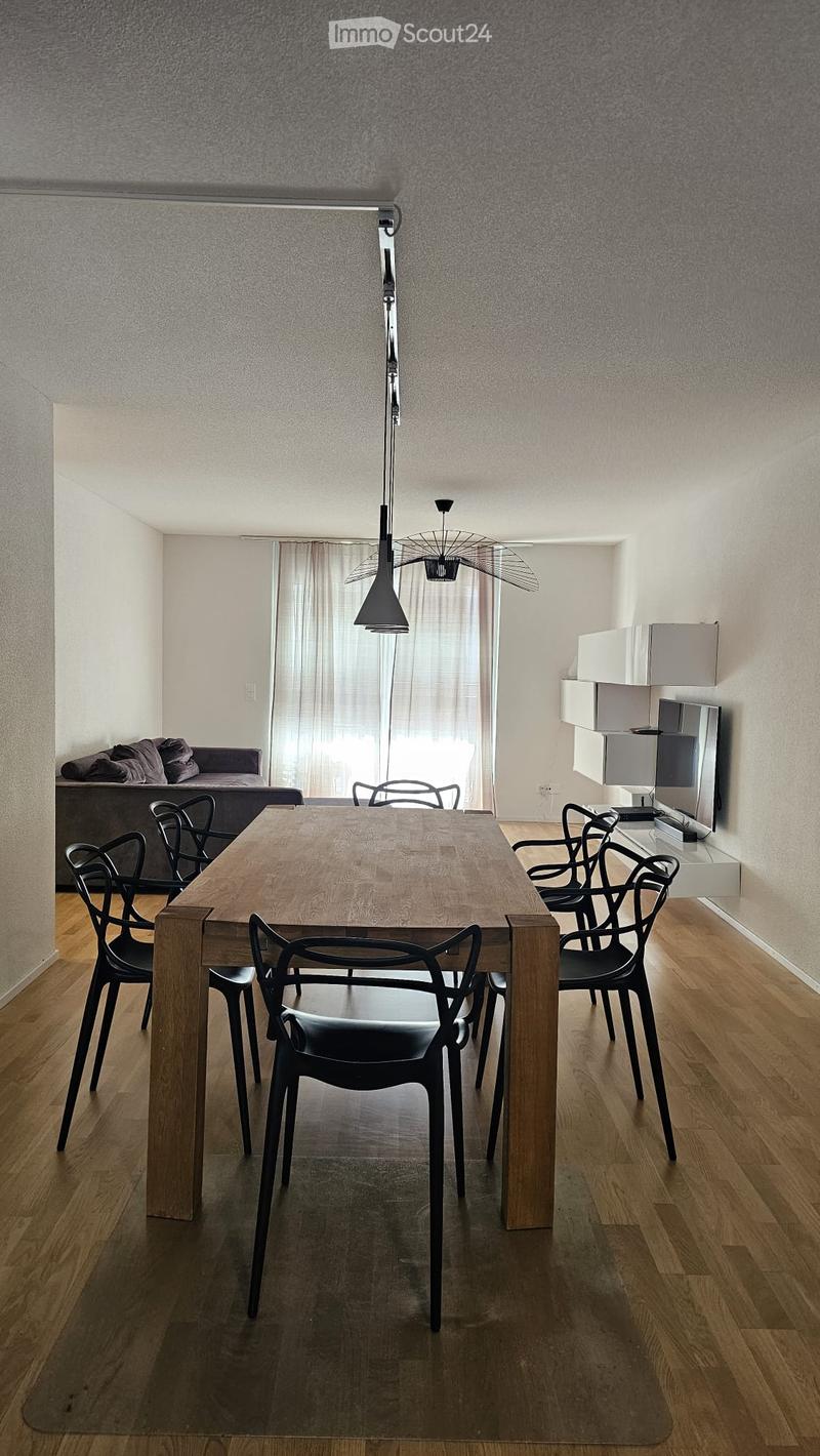 Modern dining area with a wooden dining table, black chairs, a sofa, and a large window with curtains. A mirror and cabinet are visible on the right side.