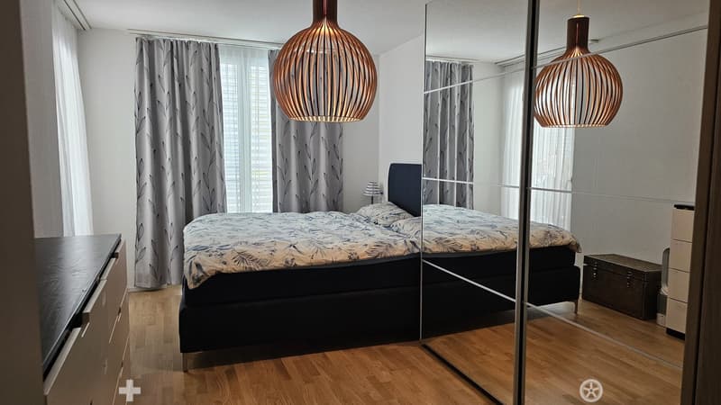 Modern bedroom with a large bed, nightstand, mirror, wardrobe, and pendant lighting.