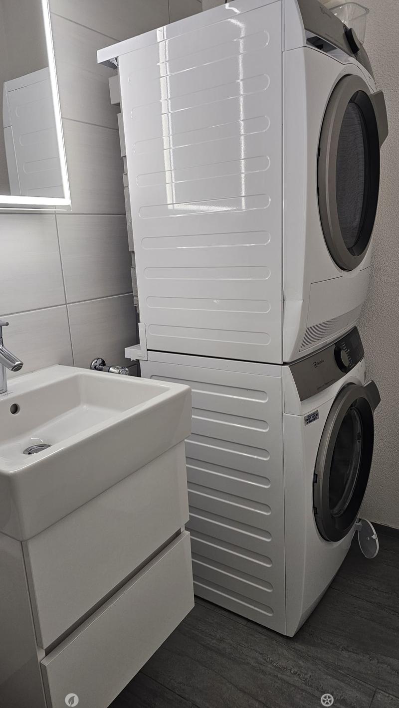 Modern bathroom with a white sink, chrome faucet, and a stacked washing machine and dryer unit.