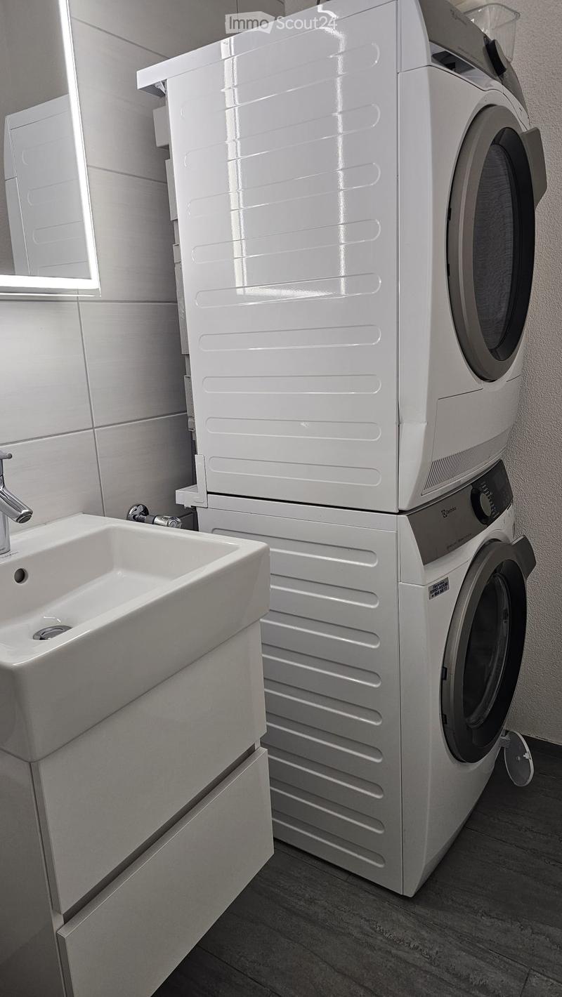 Modern bathroom with a white sink, chrome faucet, and a stacked washing machine and dryer unit.