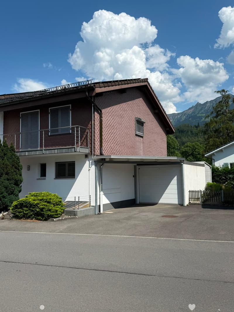Two-story house with red-tiled roof, white garage, balcony, and surrounding greenery.
