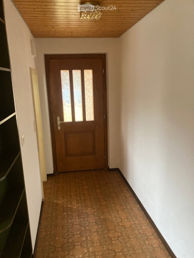 Hallway with a wooden door, tiled floor, and light fixture on the ceiling.