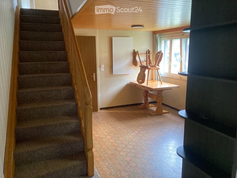 A small hallway with a staircase leading upwards, a small wooden table with a chair, and a window letting in natural light.