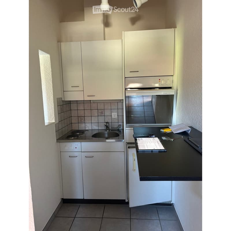 Modern kitchen with white cabinets, stainless steel oven, sink, and countertop. Includes a laptop and scissors on the counter.
