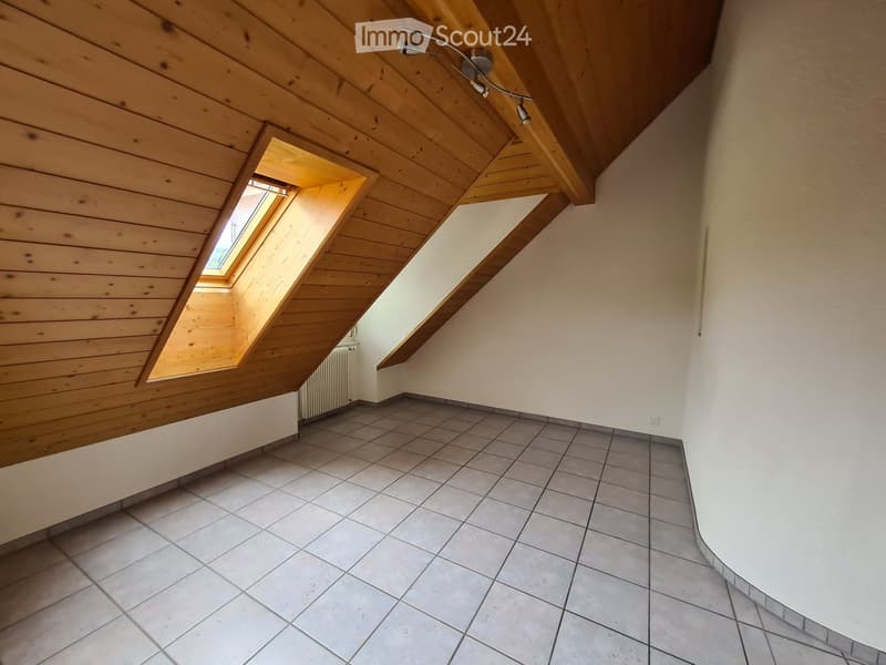 Empty attic room with wooden slanted ceiling, tiled floor, and skylight window letting in natural light.