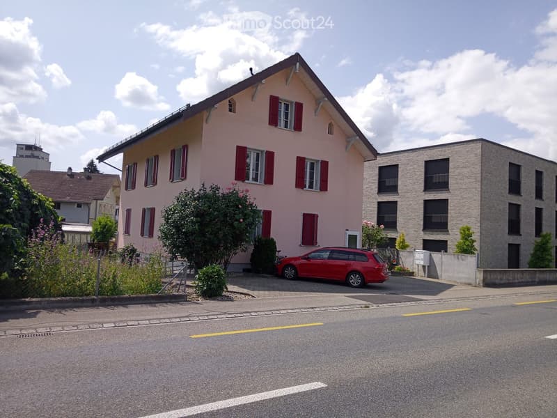 pink 2-story house with red shutters, red car parked, garden in front