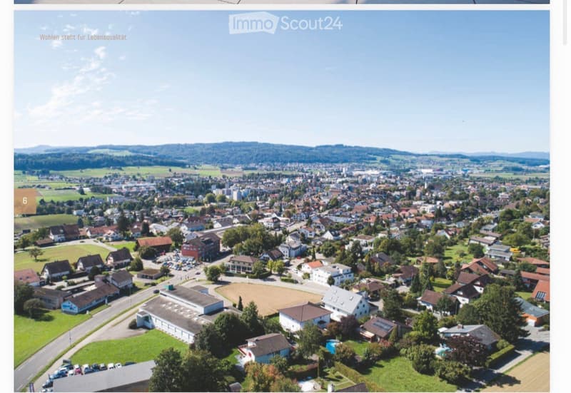 Aerial view of a suburban town with numerous houses, green spaces, and a clear sky.