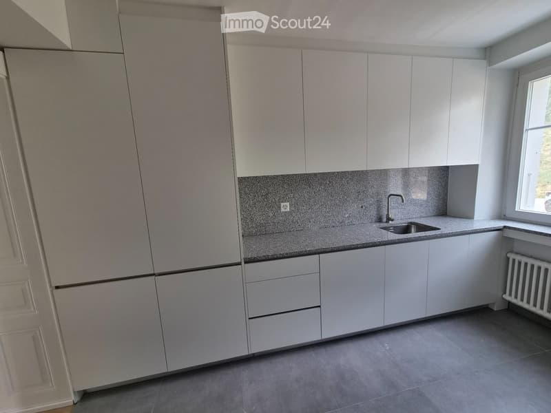 Modern kitchen with white cabinets, grey countertops, and a stainless steel sink.