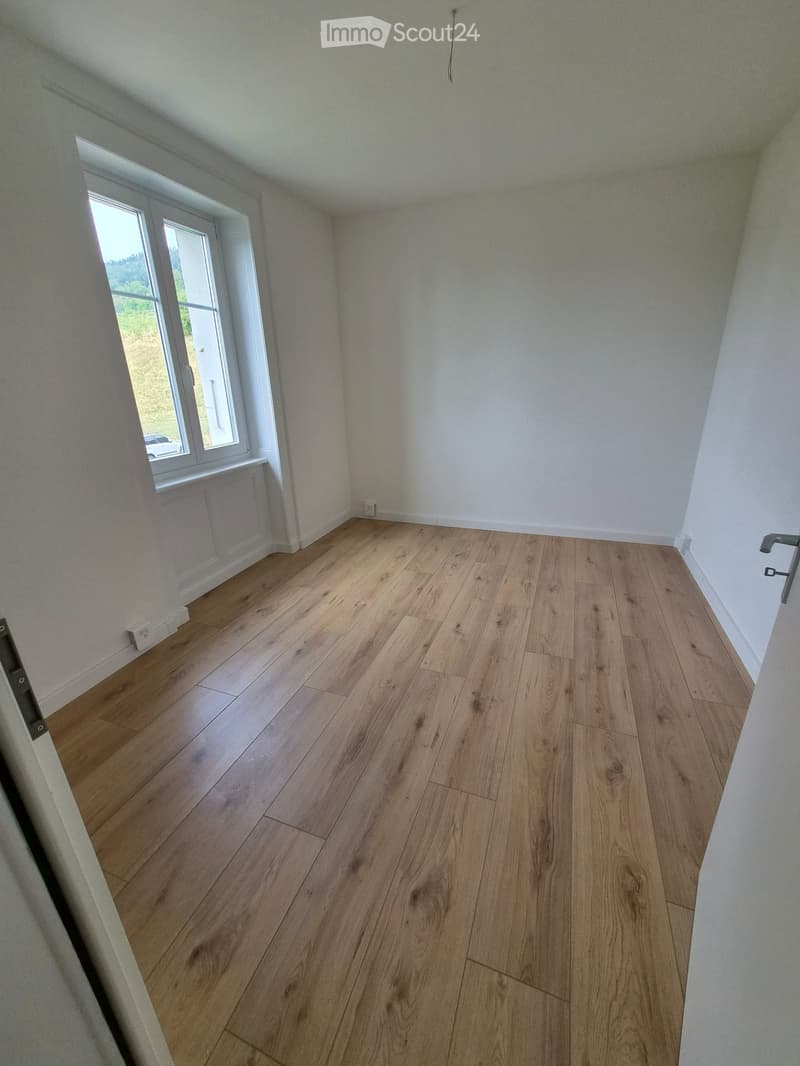 Empty room with light wooden flooring and white walls, featuring a large window with white frame and a radiator below it.