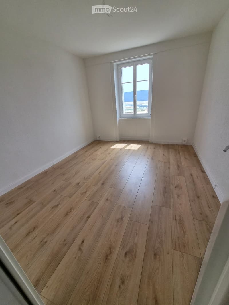Empty room with light wooden flooring and white walls, featuring a single window with a view of the outside.