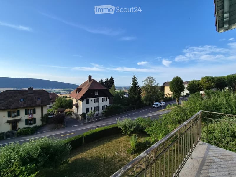 Balcony overlooking a residential street with houses, trees, and a clear blue sky.