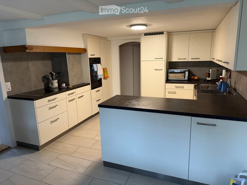 Modern kitchen with white cabinets, black countertops, and stainless steel appliances. Features include a microwave, coffee maker, and a sink with a faucet.