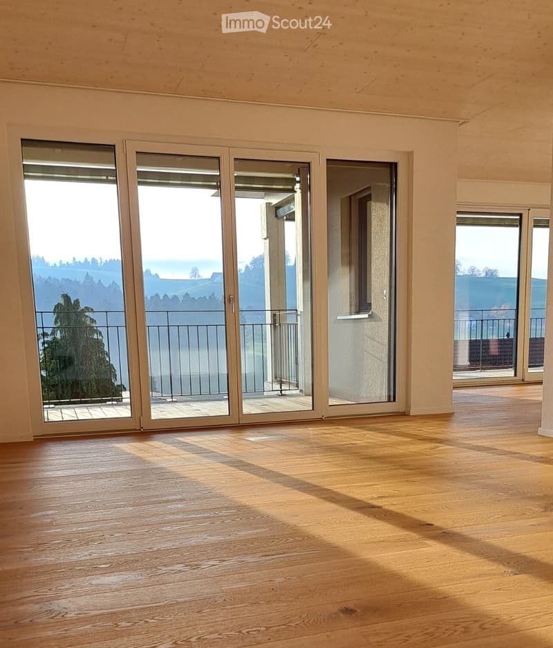 Empty room with wooden flooring and large sliding glass doors leading to a balcony with a scenic view.