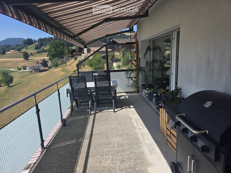 Balcony with a table, chairs, grill, and potted plants, overlooking a scenic countryside view.