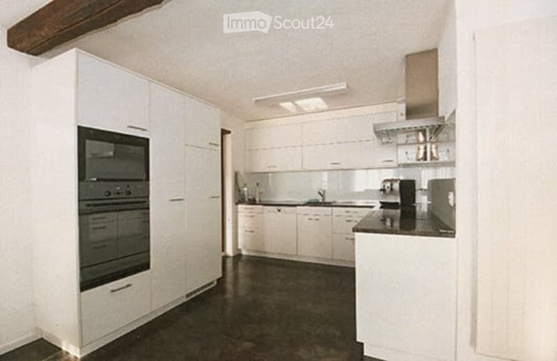 Modern kitchen with white cabinets, dark flooring, built-in oven, sink, and coffee maker.