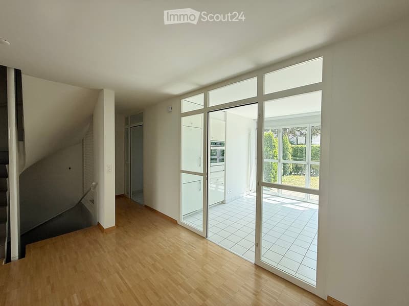 Empty room with wooden flooring, large glass sliding doors leading to a tiled patio, and a staircase visible on the left side.