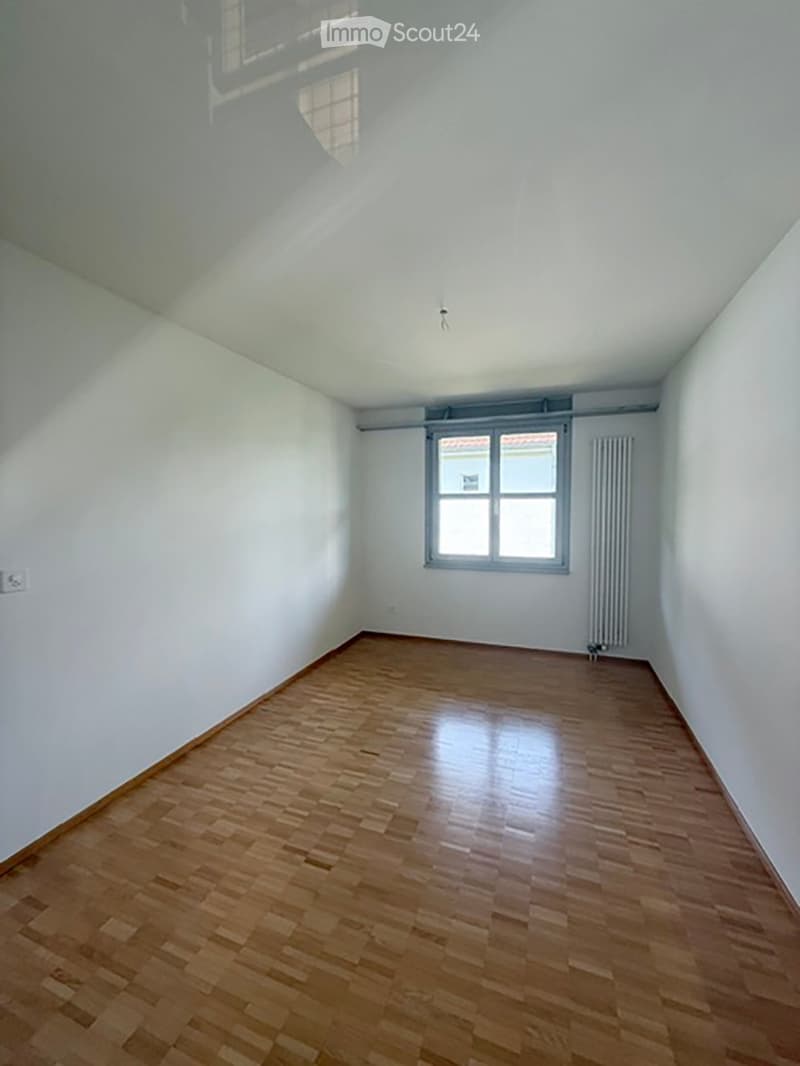 Empty room with wooden flooring, white walls, and a single window with a radiator below it.