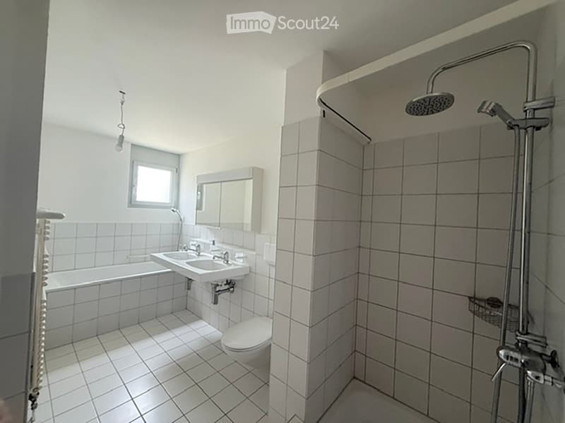 Modern bathroom with white tiled walls and floor, featuring a bathtub, sink, toilet, mirror, and a shower with a handheld sprayer.