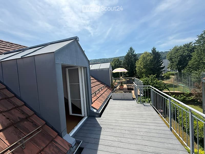 Roof terrace with wooden decking, metal railing, small shed, and outdoor furniture including a table and chairs under an umbrella.