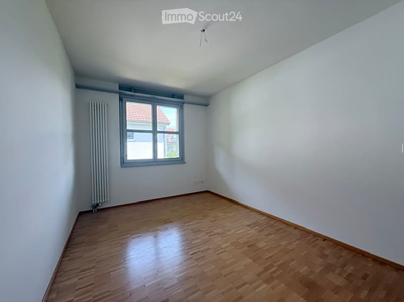 Empty room with wooden flooring, white walls, and a single window with a radiator below it.