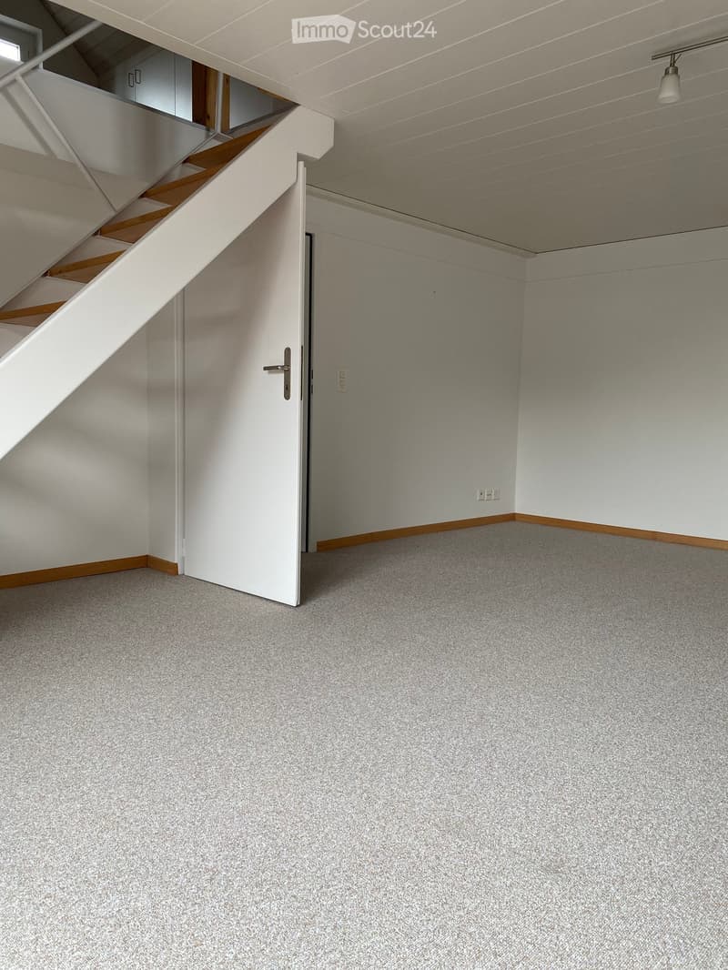 Empty room with grey carpet, white walls, and a staircase leading upwards. No furniture or equipment visible.