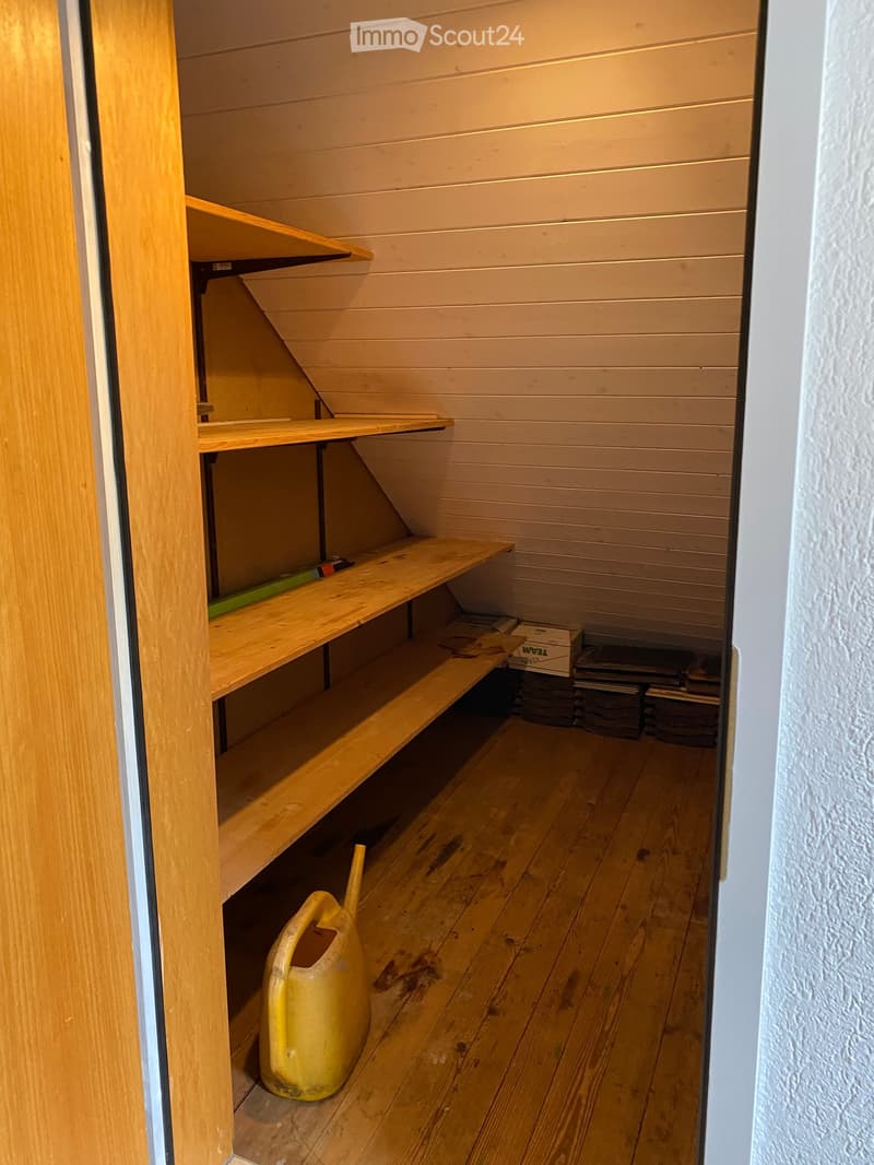 Empty wooden storage room with built-in shelves, a yellow watering can, and stacked items in the corner.