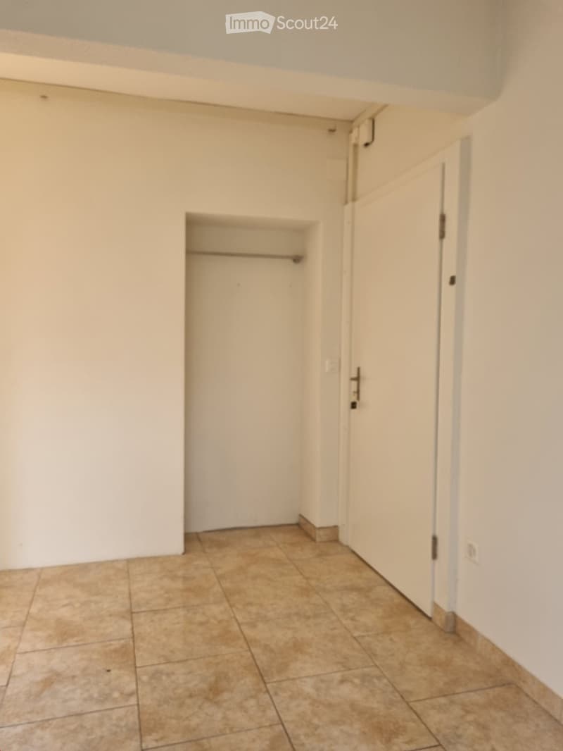 Empty hallway with beige tiled floor, white walls, and a small closet with a single shelf visible.