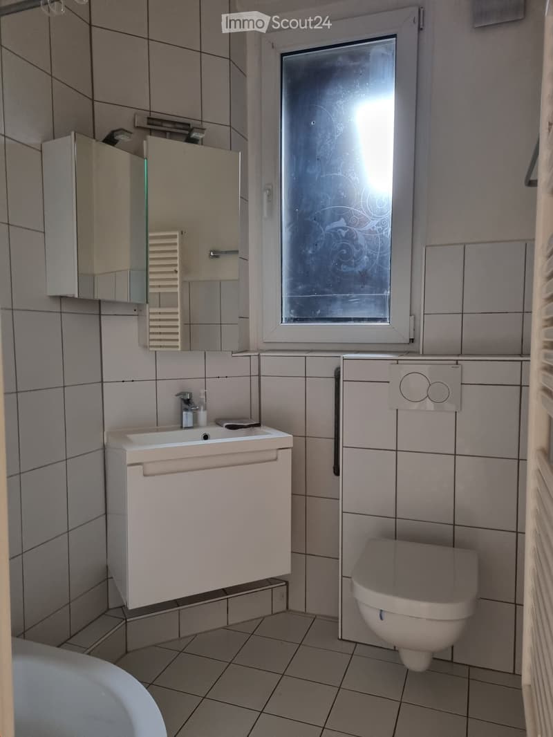 Modern bathroom with tiled walls and floor, featuring a white sink with a faucet, a toilet, a mirrored cabinet, and a radiator.