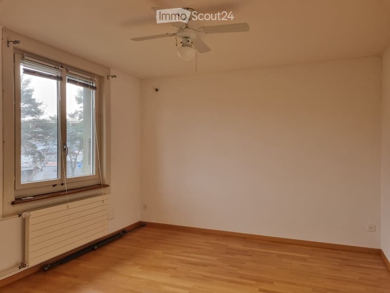 Empty room with wooden flooring, white walls, a ceiling fan, and a large window with blinds.