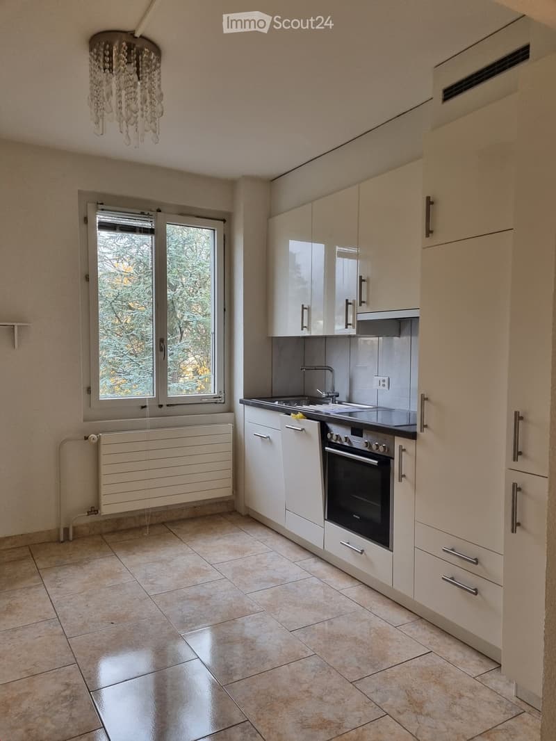 Modern kitchen with white cabinets, stainless steel oven, sink, and faucet, tiled floor, and a chandelier.
