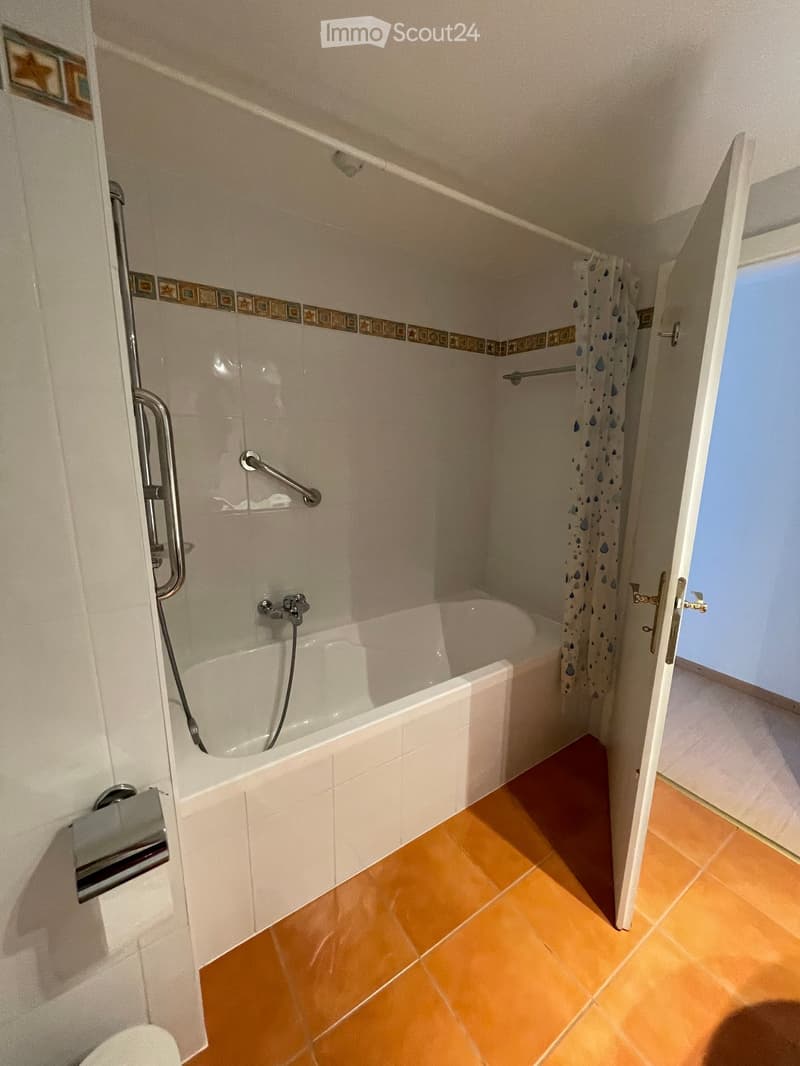 Bathroom with a white bathtub, tiled walls, a shower curtain, and a handrail for accessibility.