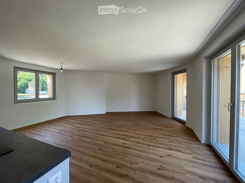 Empty room with wooden flooring, white walls, large window, and sliding glass door leading outside.