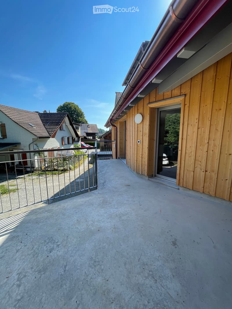 Balcony with wooden walls, metal railing, and a view of neighboring houses and a driveway.