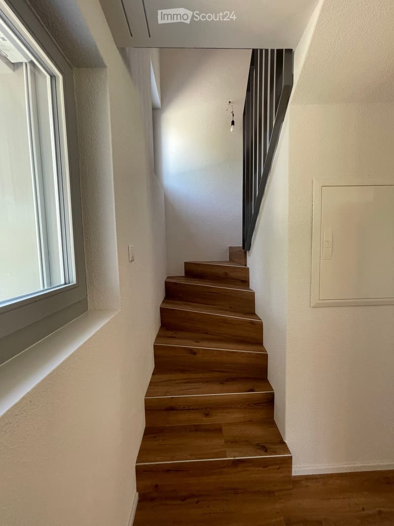Wooden staircase with modern railing, light-colored walls, and a window on the left side.