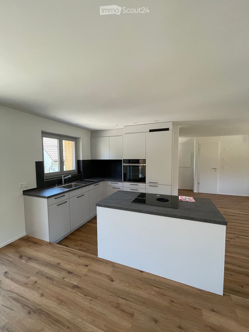 Modern kitchen with white cabinets, dark countertops, a central island, and built-in appliances including an oven and sink.