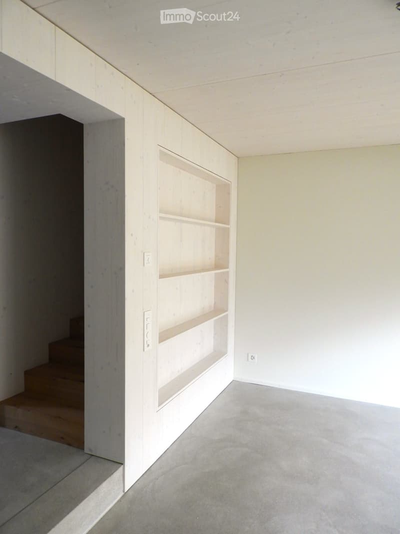 Empty room with light-colored walls, a built-in shelf unit, and a small staircase leading upwards.