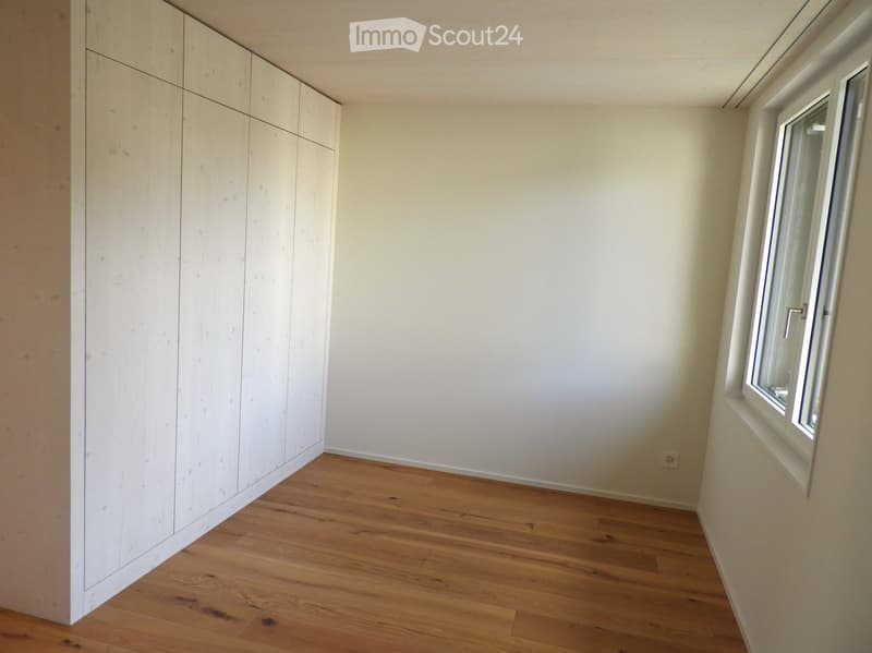 Empty room with light wooden flooring, white walls, built-in white closet, and a single window with white frame.