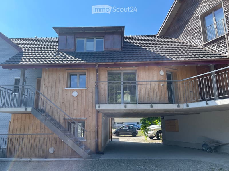Two-story wooden house with balconies, tiled roof, and attached garage. Stairs lead to the upper level.