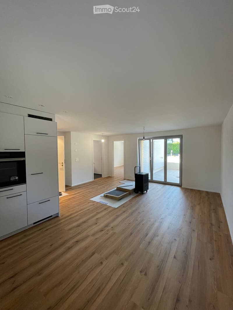 Empty room with wooden flooring, white walls, and a large sliding glass door leading to an outdoor area. There is a cabinet on the left side and a small cart near the door.