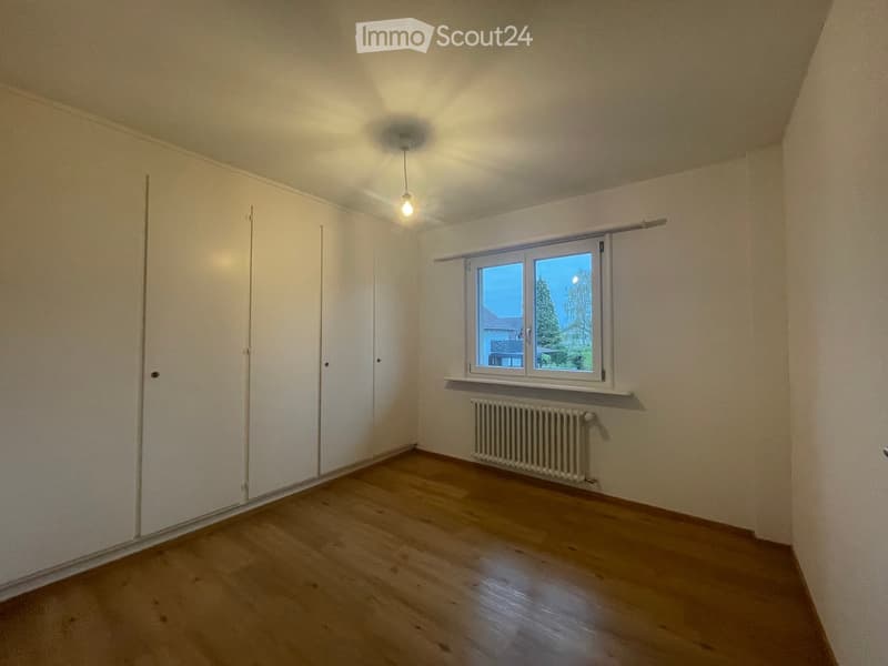 Empty room with wooden flooring, white walls, a window with a view, a radiator, and built-in wardrobes.