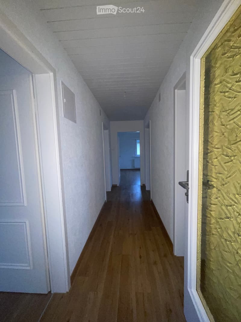 Empty hallway with wooden flooring, white walls, and multiple doors on both sides.
