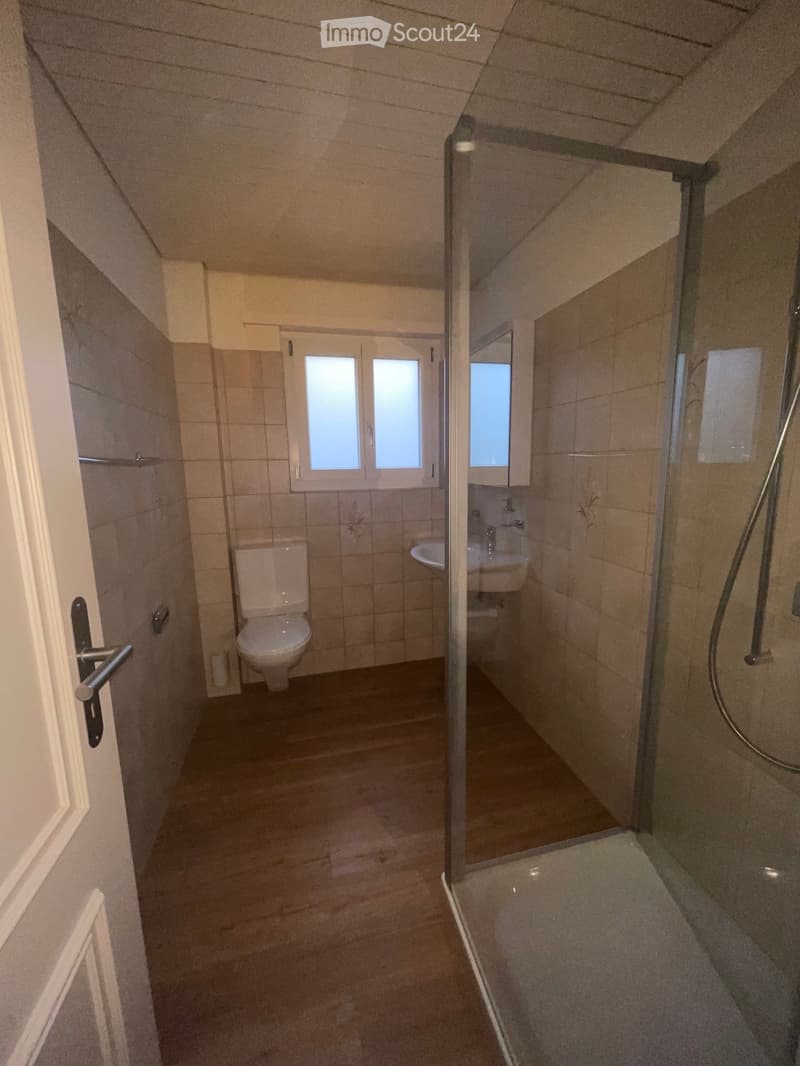 Bathroom with a toilet, sink, and glass-enclosed shower. The room has tiled walls and a window above the sink.