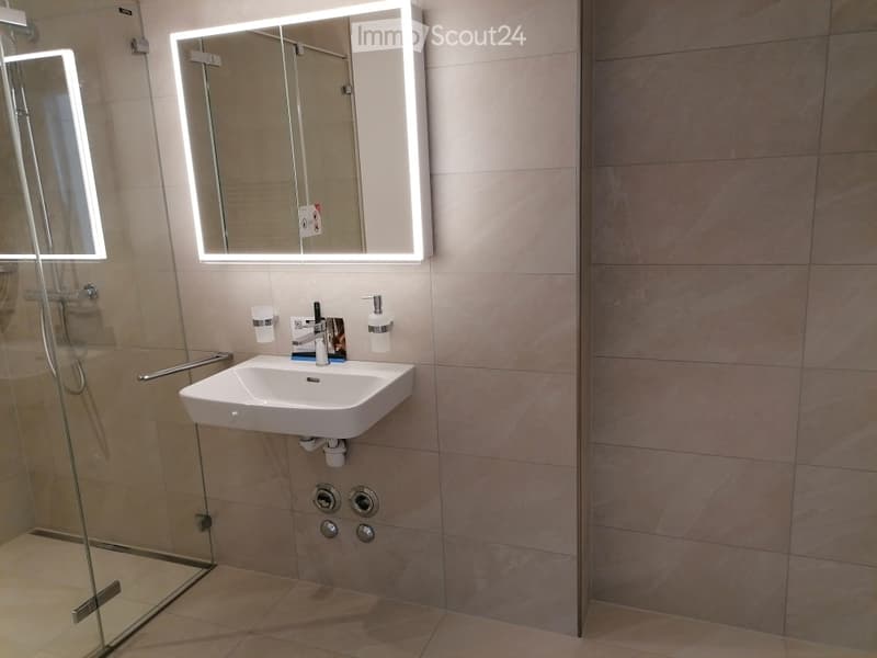 Modern bathroom with a white sink, illuminated mirror, glass shower enclosure, and tiled walls.