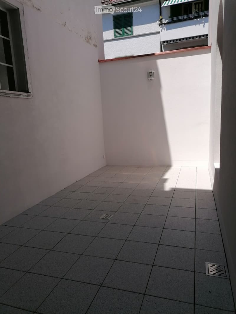 Empty outdoor patio with tiled flooring, white walls, and a small window on one side.