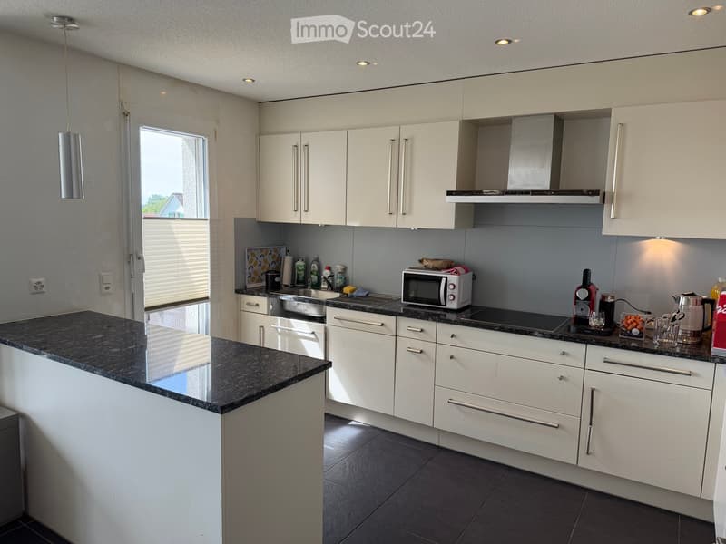 Modern kitchen with white cabinets, dark granite countertops, and stainless steel appliances including a microwave, coffee maker, and teapot. Features a central island and built-in lighting.