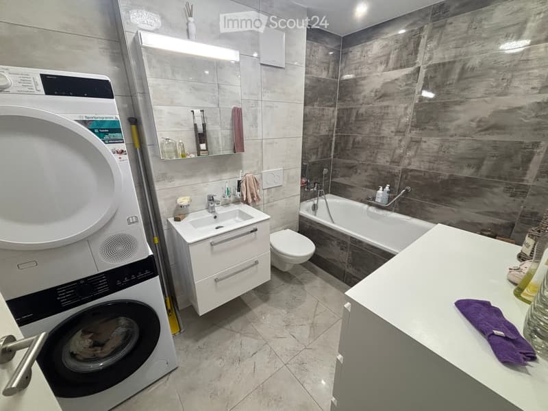 Modern bathroom with a washing machine, sink, toilet, bathtub, and a large mirror above the sink.